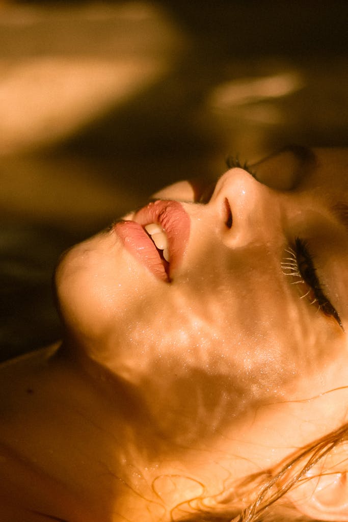 Close-up of a woman's face with sunlight casting shadows, highlighting lips and peaceful expression.